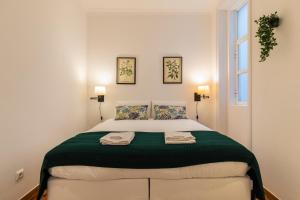 a white bedroom with a large bed with green blanket at SALDANHA POMBALINE RESIDENCE in Lisbon