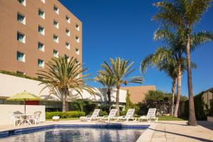 einen Pool mit Stühlen und Palmen vor einem Hotel in der Unterkunft Fiesta Inn Tijuana Otay Aeropuerto in Tijuana