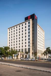 un gran edificio blanco en una calle con coches aparcados delante en Fiesta Inn Merida en Mérida