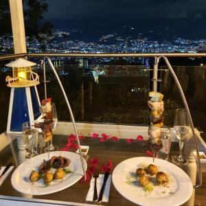 a table with two plates of food on a balcony at night at HOTEL BOUTIQUE EL FARO BY AROMAX in Medellín