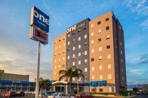 un bâtiment d'hôtel avec des voitures garées dans un parking dans l'établissement One Monterrey Aeropuerto, à Monterrey