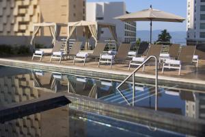 een groep stoelen en een parasol naast een zwembad bij Fiesta Inn Puerto Vallarta Isla in Puerto Vallarta