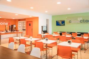 a restaurant with white tables and orange chairs at One Guadalajara Expo in Guadalajara