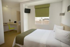 1 dormitorio con cama blanca, escritorio y ventana en One Aguascalientes Sur en Aguascalientes