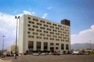un grand bâtiment blanc avec des voitures garées dans un parking dans l'établissement Fiesta Inn Pachuca Gran Patio, à Pachuca