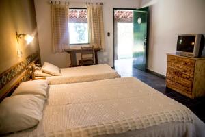a bedroom with two beds and a television and a door at Pousada Flor da Serra in Cruzeiro