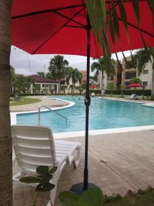 a red umbrella and a chair next to a swimming pool at Paradise 3 cerro Altos in Santiago de los Caballeros