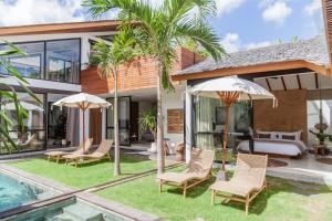 a villa with a swimming pool with chairs and umbrellas at Beyond Bespoke Villas in Seminyak