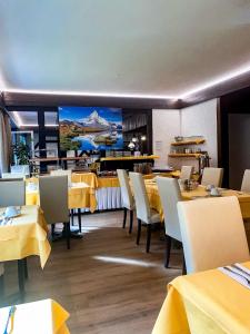 ツェルマットにあるホテル アドニスの黄色のテーブルと椅子、大きな壁画のあるレストラン