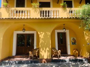 une maison jaune avec deux portes et des chaises sur une terrasse dans l'établissement Villa Le Gemelle Dell'Alcantara, à Motta Camastra