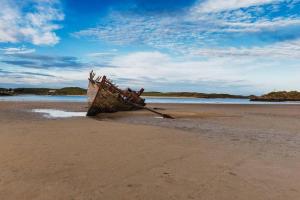 an old boat sitting on the sand on a beach at Luí na Gréine in Gweedore