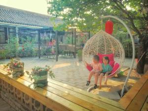 two children sitting in a swing in a backyard at Beijing Badaling Great Wall Cao’s Courtyard Hostel in Yanqing