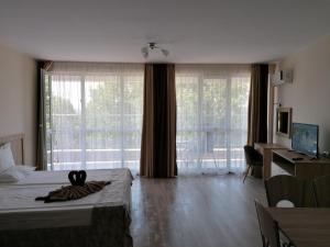 a bedroom with a bed and a desk and windows at Apart Allure Dobi in Primorsko