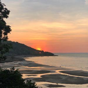 a sunset on a beach with the sun setting over the ocean at Banyan Bay Villas in Ko Jum