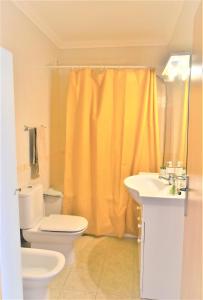 a bathroom with a toilet and a yellow shower curtain at Ritta's house in Albufeira