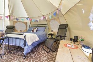 Bett in einem Zelt mit 2 Stühlen und einem Tisch in der Unterkunft Pitch Perfect Glamping Norfolk in Little Hautbois