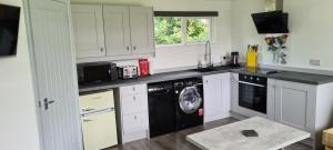 uma cozinha com armários brancos e uma máquina de lavar louça preta em Forget-Me-Not 114 Woodlands Park New Quay em New Quay