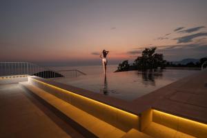 a woman standing on the edge of a swimming pool at sunset at Vivid Blue Serenity Resort in Sveti Stefan