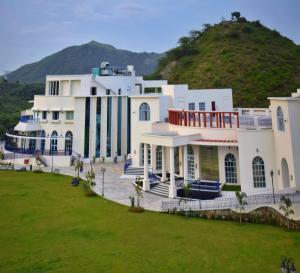 a large white building with a hill in the background at Ramee Royal Resorts & Spa - Udaipur in Udaipur