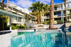 a swimming pool with palm trees in front of a building at The Beach Cabarita in Cabarita Beach