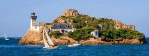 a sail boat in the water with a lighthouse at ty_yaouen maison de vacances in Carantec