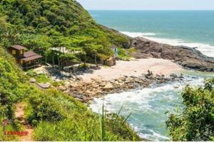 a beach with a house on a hill next to the ocean at Pousada Fiedler E Anacleto in Penha