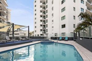 a swimming pool with chairs and a building at Key Largo Maroochydore in Maroochydore