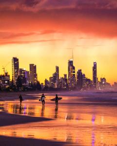 3 personnes marchant sur la plage avec leurs planches de surf dans l'établissement Nobby Beach Holiday Village, à Gold Coast