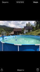 a large blue swimming pool with a house in the background at Zelenyj Raj in Pashkivtsi