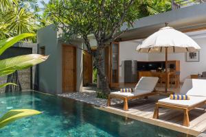 a pool with chairs and an umbrella next to a house at KoenoKoeni Villa in Seminyak