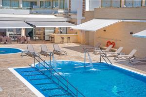 een groot zwembad met stoelen en een gebouw bij Hotel Biniamar in Cala Millor