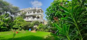 une grande maison blanche avec une pelouse devant elle dans l'établissement IbisHouse Farm Stay, à Bharatpur