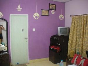 Habitación con pared morada, TV y puerta. en Neel Nirjaney Resorts en Mandarmoni