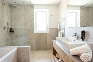 ein Badezimmer mit einem Waschbecken, einer Badewanne und einem Spiegel in der Unterkunft Hotel Hofer in Dorf Tirol
