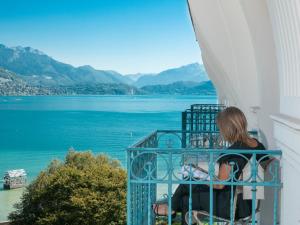 a woman sitting on a balcony looking at the water at Impérial Palace in Annecy