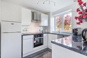 a kitchen with white cabinets and a black counter top at 2 Bed Flat, Dedicated workspace, Parking, 4KTV in London
