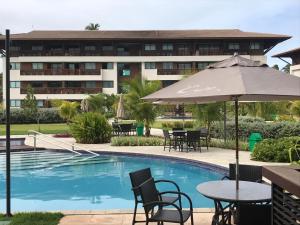una piscina dell'hotel con tavoli, sedie e ombrellone di Cupe Beach Living Flat a Porto De Galinhas