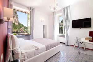 Cette chambre blanche dispose d'un lit, d'une table et d'une fenêtre. dans l'établissement Valle d'Amalfi Suites, à Amalfi