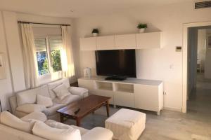 uma sala de estar com mobiliário branco e uma televisão de ecrã plano em Precioso apartamento muy cerca de la playa em Chiclana de la Frontera