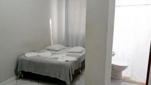 a small white bedroom with a bed and a toilet at Hotel Bella Júlia in Joinville