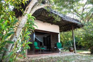 un cottage avec un toit de chaume et des chaises vertes dans l'établissement Fumba Beach Lodge, à Fumba