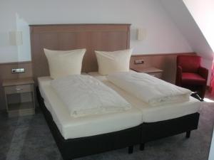 1 cama con 2 almohadas y silla roja en Pension zur Traube 3 Sterne, en Oberschwarzach