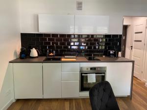 a kitchen with white cabinets and a black tile wall at Apartament MATEO in Malbork