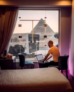 a man sitting at a desk with a laptop in front of a window at Cleopatra Pyramids View in Cairo