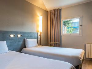 a hotel room with two beds and a window at ibis budget Senlis in Senlis