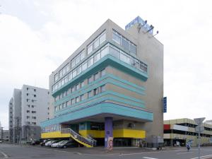 wysoki budynek z samochodami zaparkowanymi przed nim w obiekcie Tabist Hotel Tetora Hakodate Station w mieście Hakodate
