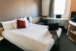 una habitación de hotel con una gran cama blanca con almohadas rojas en ibis Newcastle, en Newcastle