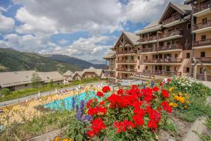 a resort with a pool and flowers in the foreground at Résidence Pierre & Vacances Le Thabor in Valmeinier