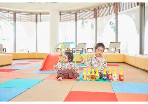 dos niños sentados en el suelo en una sala de juegos en Hotel Mahaina Wellness Resorts Okinawa, en Motobu