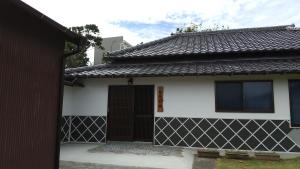 Biały i czarny dom z czarnymi drzwiami w obiekcie 築100年の宿【はぶの家】 w mieście Oshima